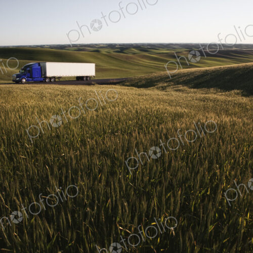 Commercial truck driving though wheat fields of eastern Washington, USA at sunset.