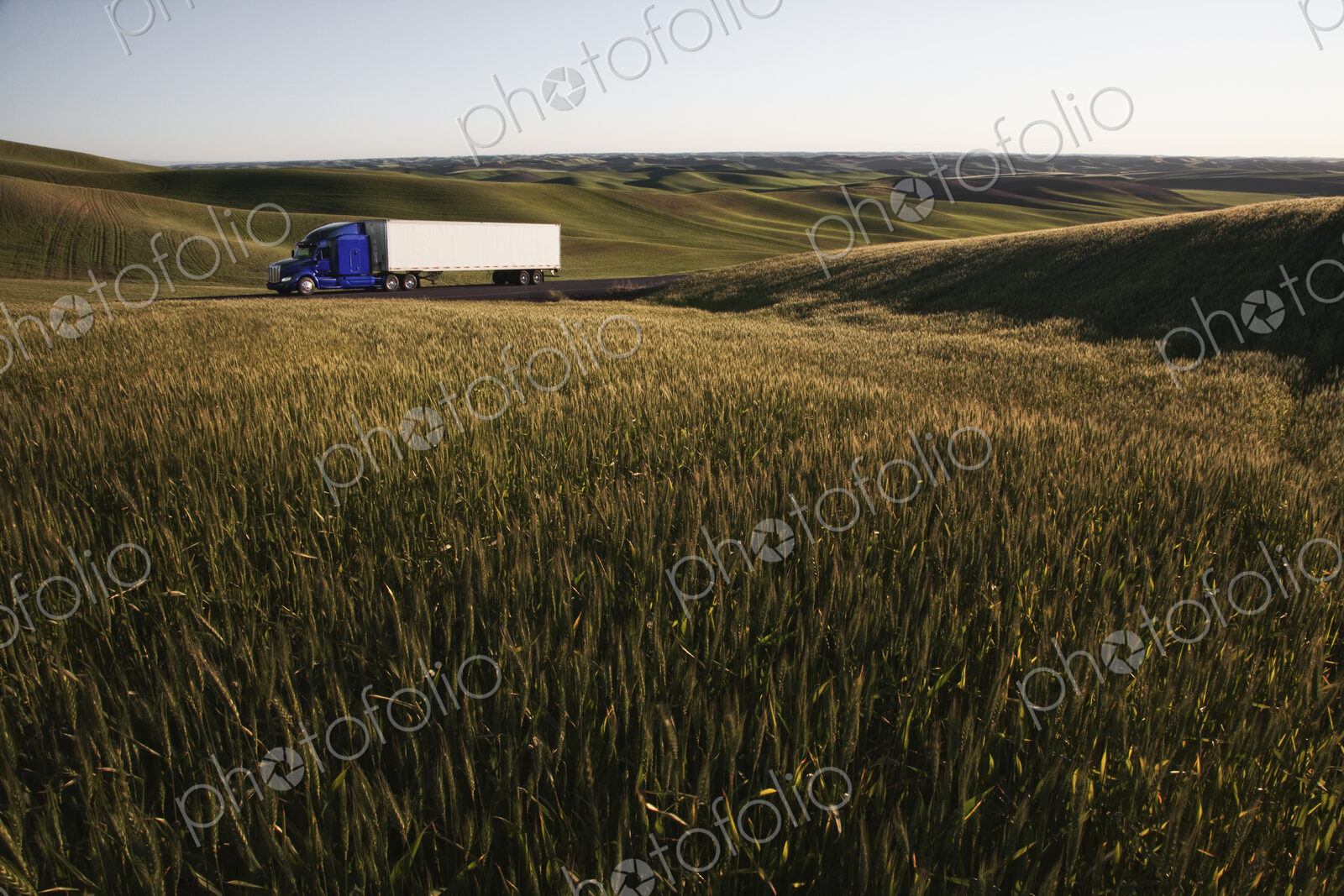 Commercial truck driving though wheat fields of eastern Washington, USA at sunset.