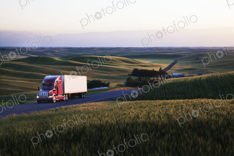 Commercial truck driving though wheat fields of eastern Washington, USA at sunset.