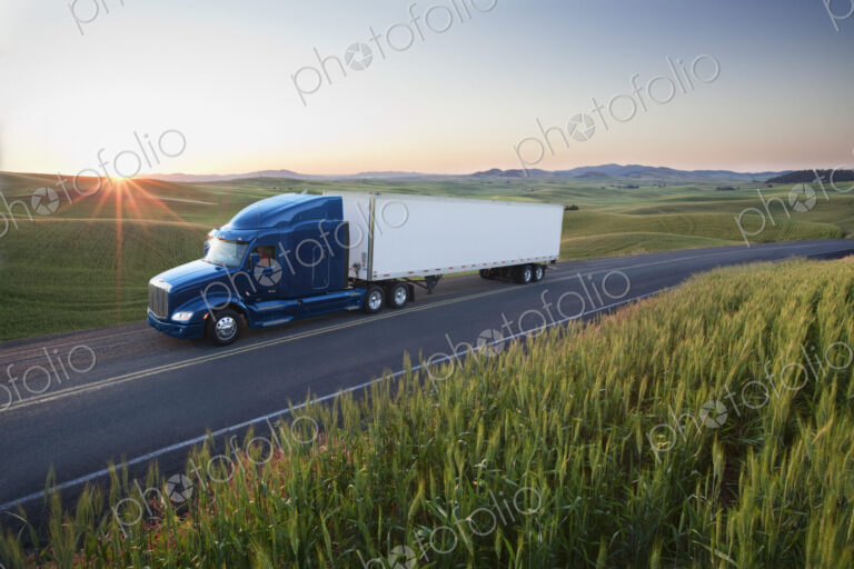 Commercial truck driving though wheat fields of eastern Washington, USA at sunset.