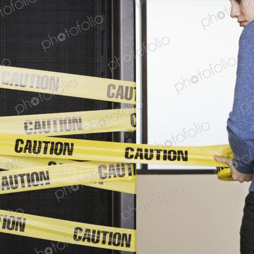 Computer server rack being wrapped with yellow caution tape by a caucasian woman. Computer server rack being wrapped with yellow caution tape by a caucasian woman.