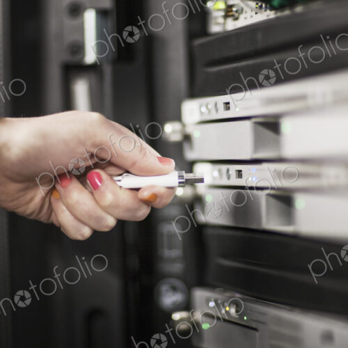 Computer techniican inserting thumb drive into a server in a server farm. Computer techniican inserting thumb drive into a server in a server farm.