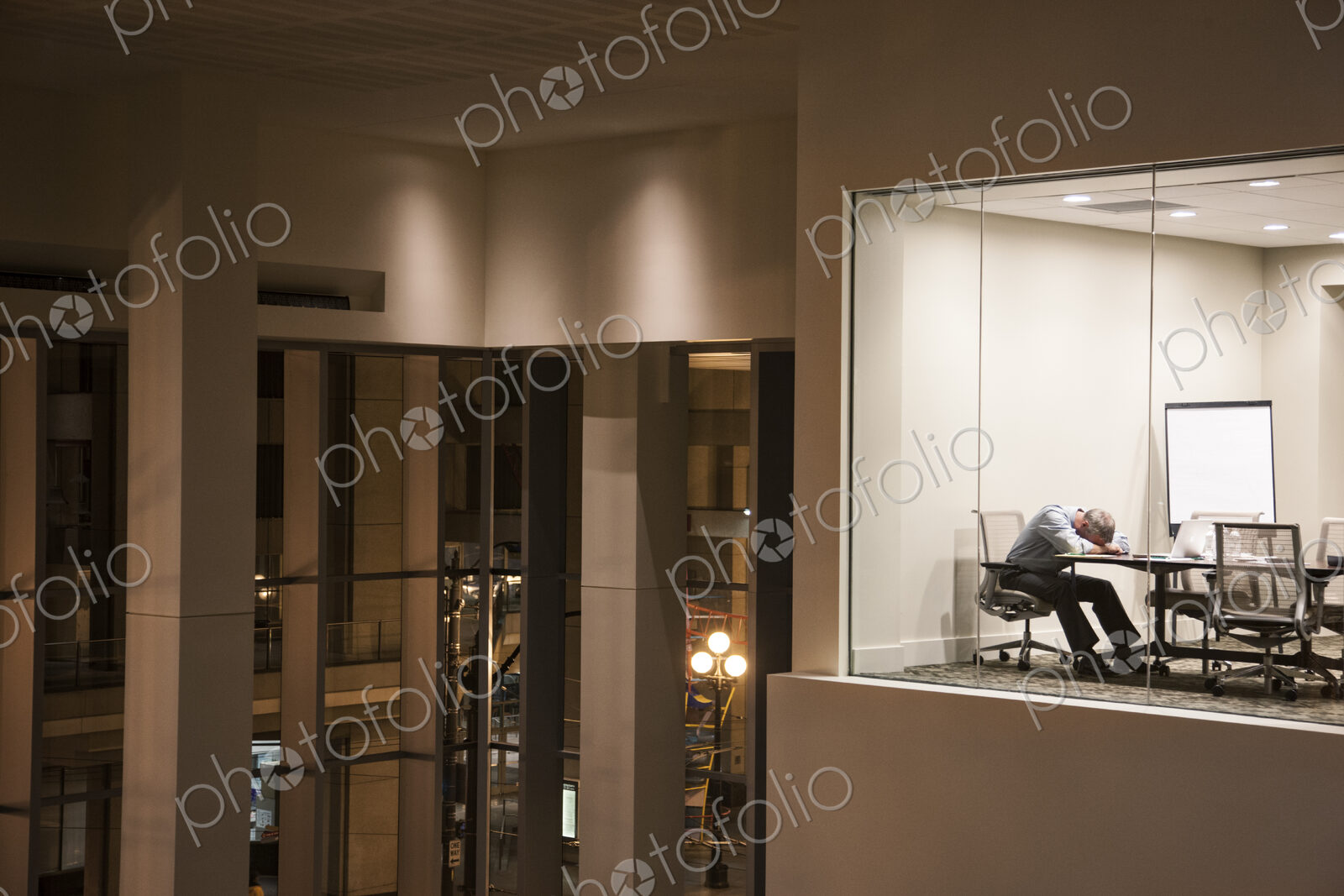 Conference room at night with a single businessman asleep at a conference table.