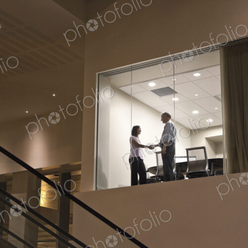 Conference room at night with two business people at work at a conference table.