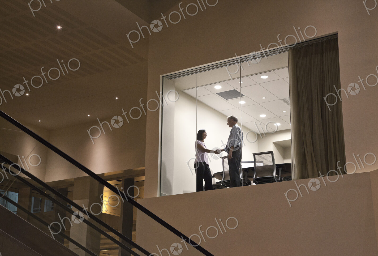 Conference room at night with two business people at work at a conference table.