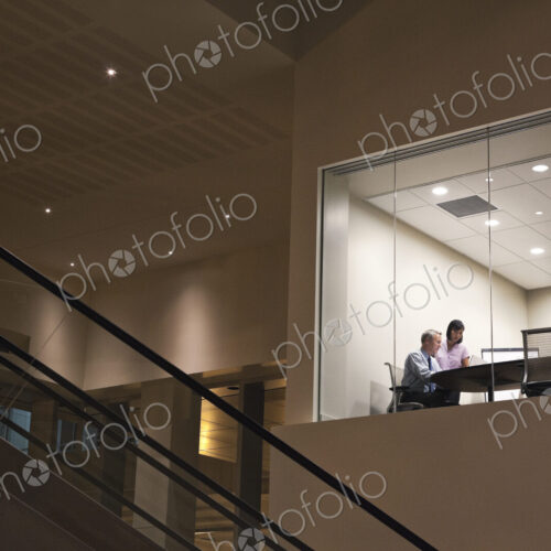Conference room at night with two business people at work at a conference table.
