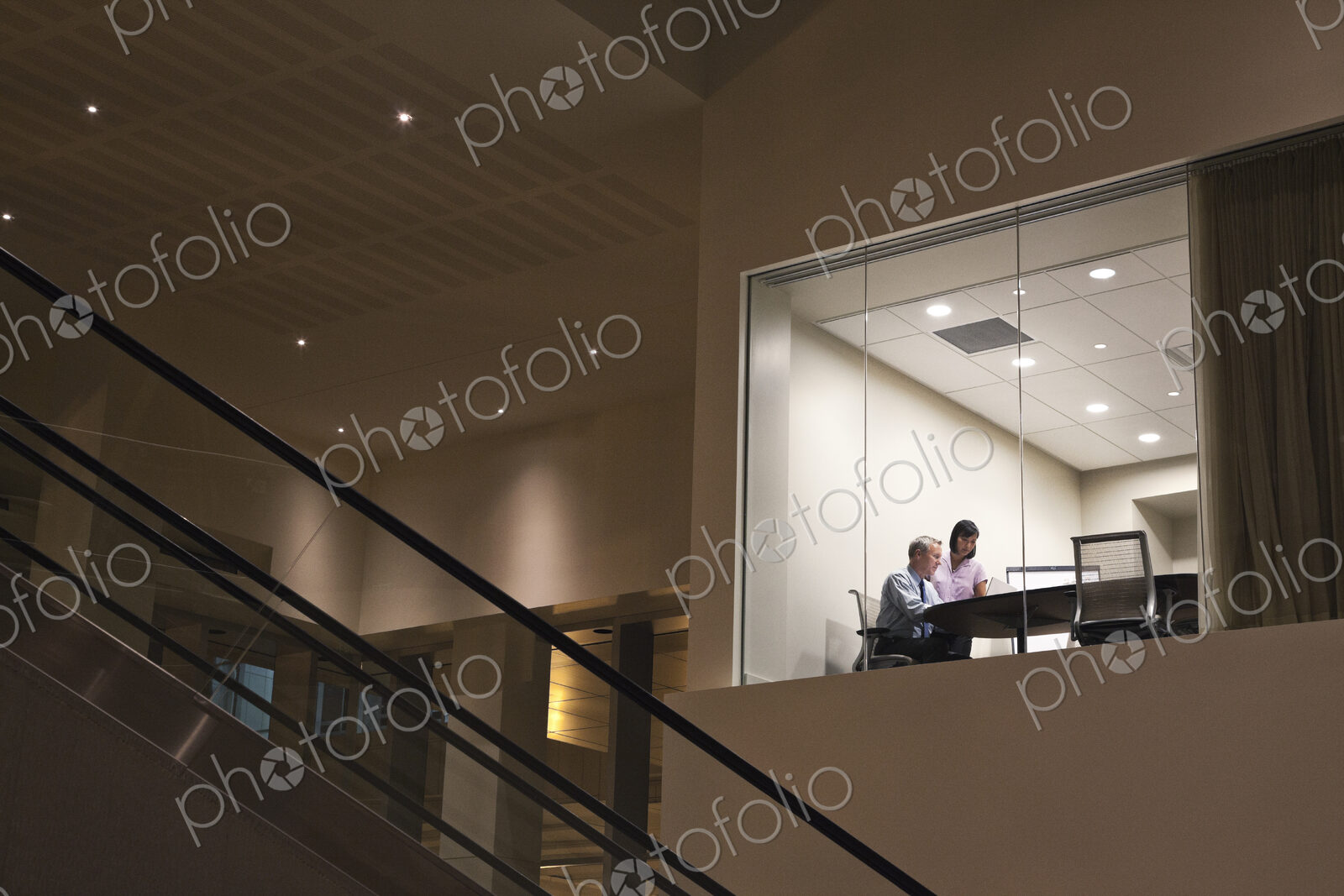 Conference room at night with two business people at work at a conference table.