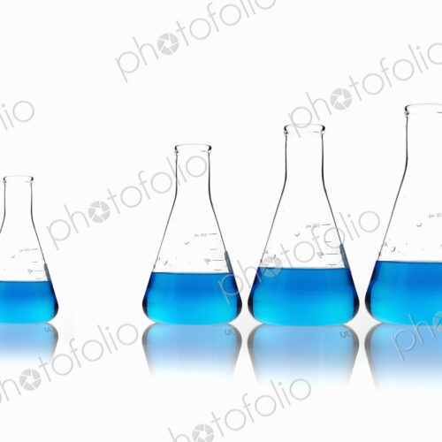 Conical glass scientific flasks holding blue liquids. Lined up in size order, with one… Conical glass scientific flasks holding blue liquids. Lined up in size order, with one…