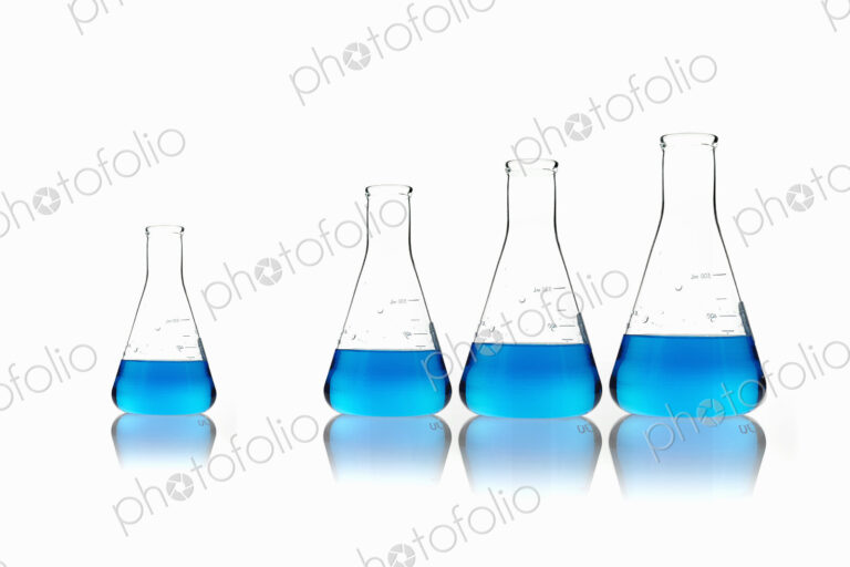 Conical glass scientific flasks holding blue liquids. Lined up in size order, with one…