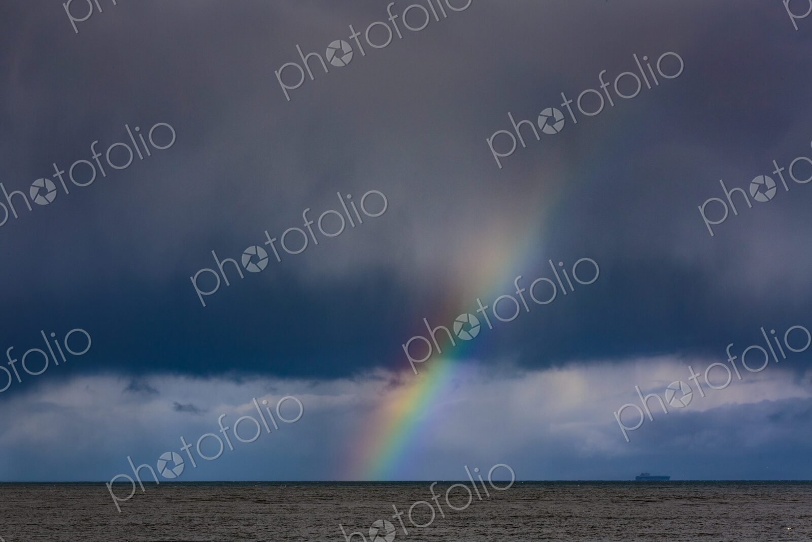 Container ship and Rainbow over water with dark storm clouds on the Strait of Juan de…