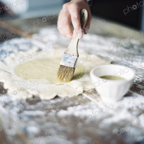 Cook rolling out pastry on a table top and brushing it with egg wash. Cook rolling out pastry on a table top and brushing it with egg wash.
