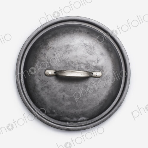 Cookware, a black round pot lid, a well used dented piece of cookware. Cookware, a black round pot lid, a well used dented piece of cookware.