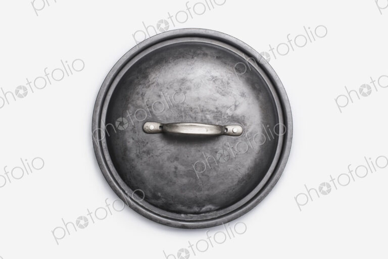 Cookware, a black round pot lid, a well used dented piece of cookware.