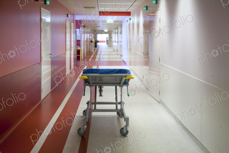Corridor and waiting areas of a modern hospital with seating, a trolley bed wih blue…