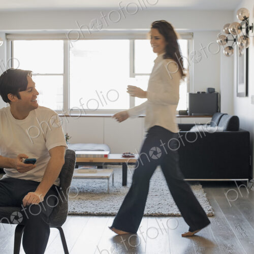 Couple at Home, Man using smartphone, Woman walking past Couple at Home, Man using smartphone, Woman walking past