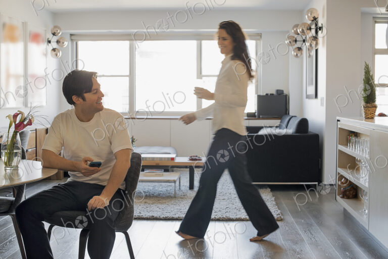 Couple at Home, Man using smartphone, Woman walking past