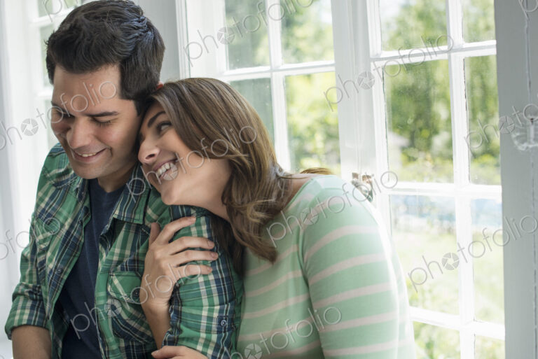 Couple embracing by a window.