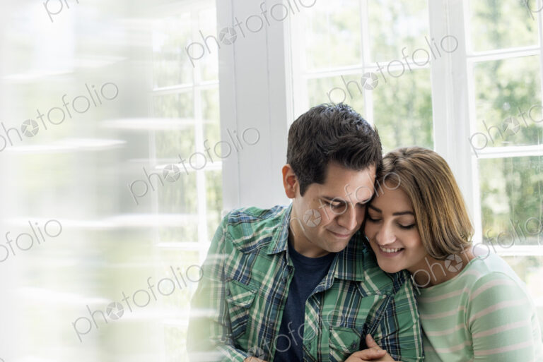 Couple embracing by a window.