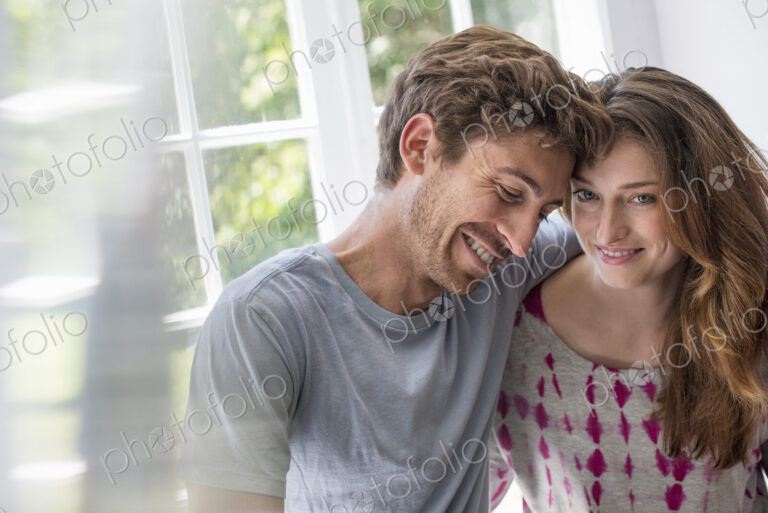 Couple embracing by a window.