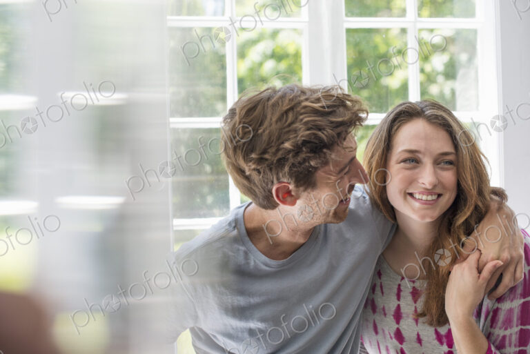 Couple embracing by a window.