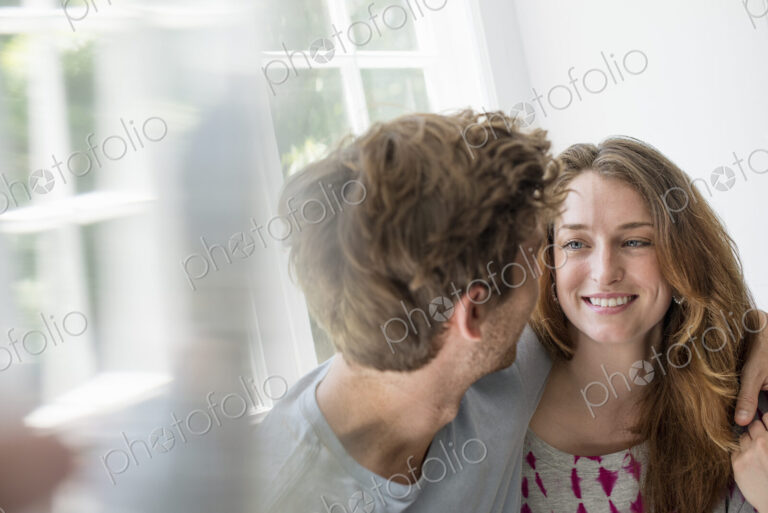 Couple embracing by a window.