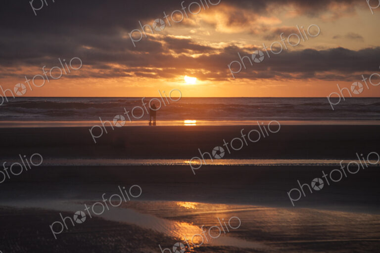 Couple hugging on Cannon Beach with dramatic cloudy sky at sunset.