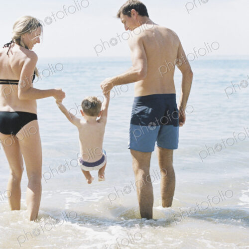Couple playing with their son on a sandy beach by the ocean.