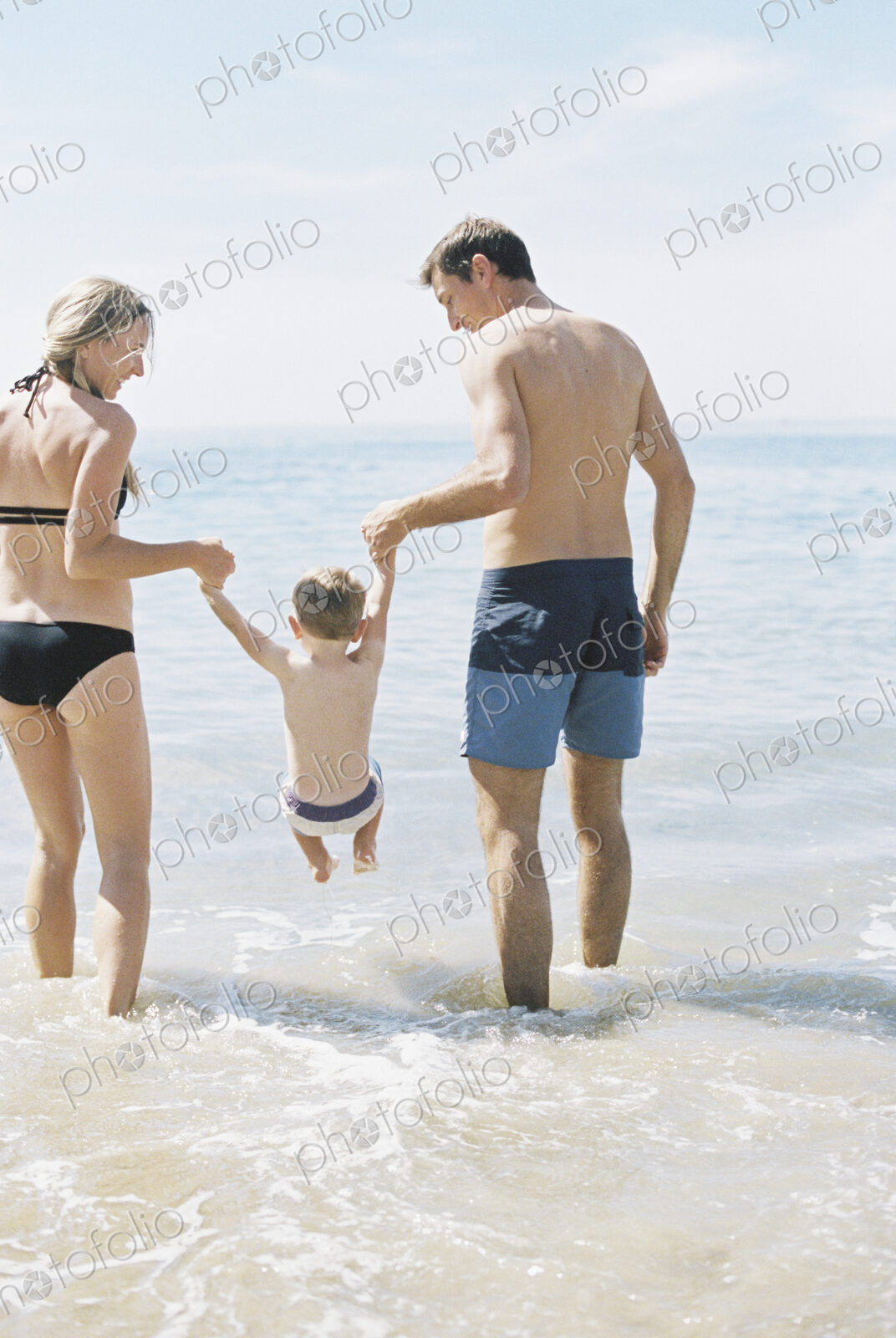 Couple playing with their son on a sandy beach by the ocean.