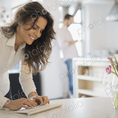 Couple relaxing at home, woman using keyboard, man using smartphone Couple relaxing at home, woman using keyboard, man using smartphone