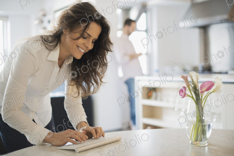 Couple relaxing at home, woman using keyboard, man using smartphone