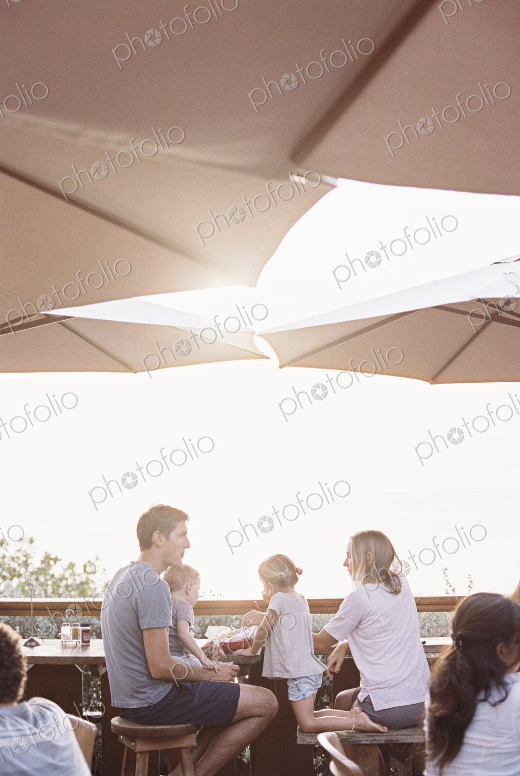 Couple sitting under a parasol in a restaurant with their son and daughter.