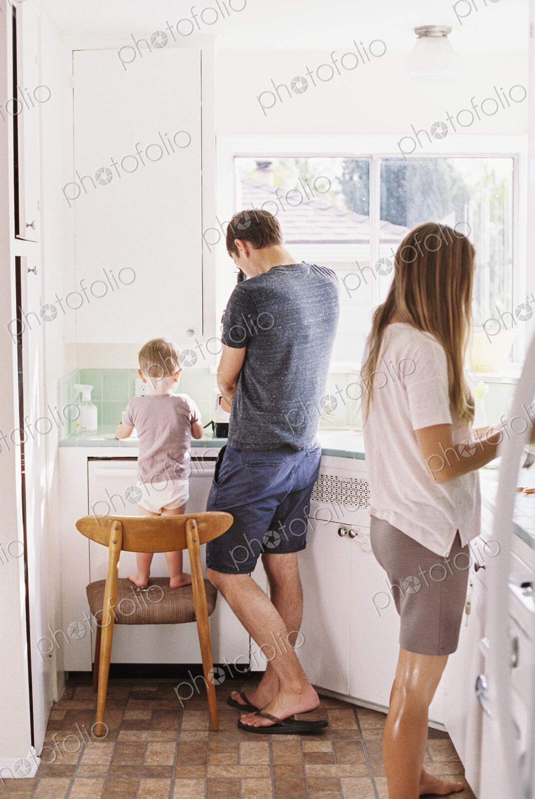 Couple standing in a kitchen, their son standing on a chair beside them.