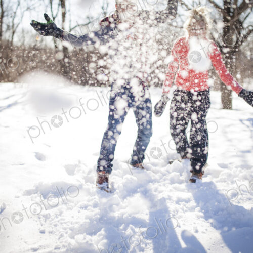 Couple throwing snowball at the camera in park.