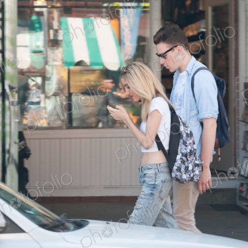 Couple walking on sidewalk, woman looking down at her phone, texting while walking. Couple walking on sidewalk, woman looking down at her phone, texting while walking.