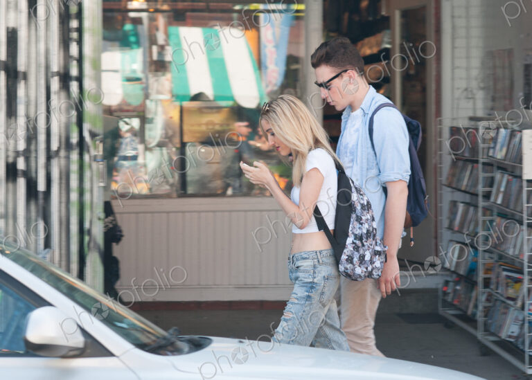 Couple walking on sidewalk, woman looking down at her phone, texting while walking.
