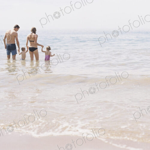 Couple with their son and daughter, A family standing in shallow water off the beach.