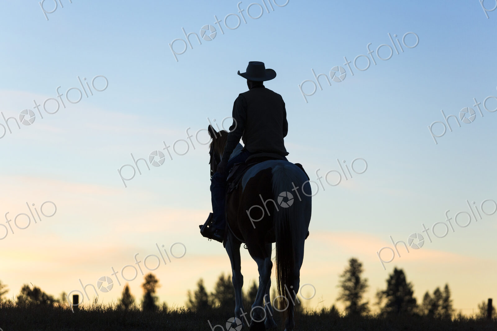 Cowboy riding on horseback in a Prairie landscape at sunset.