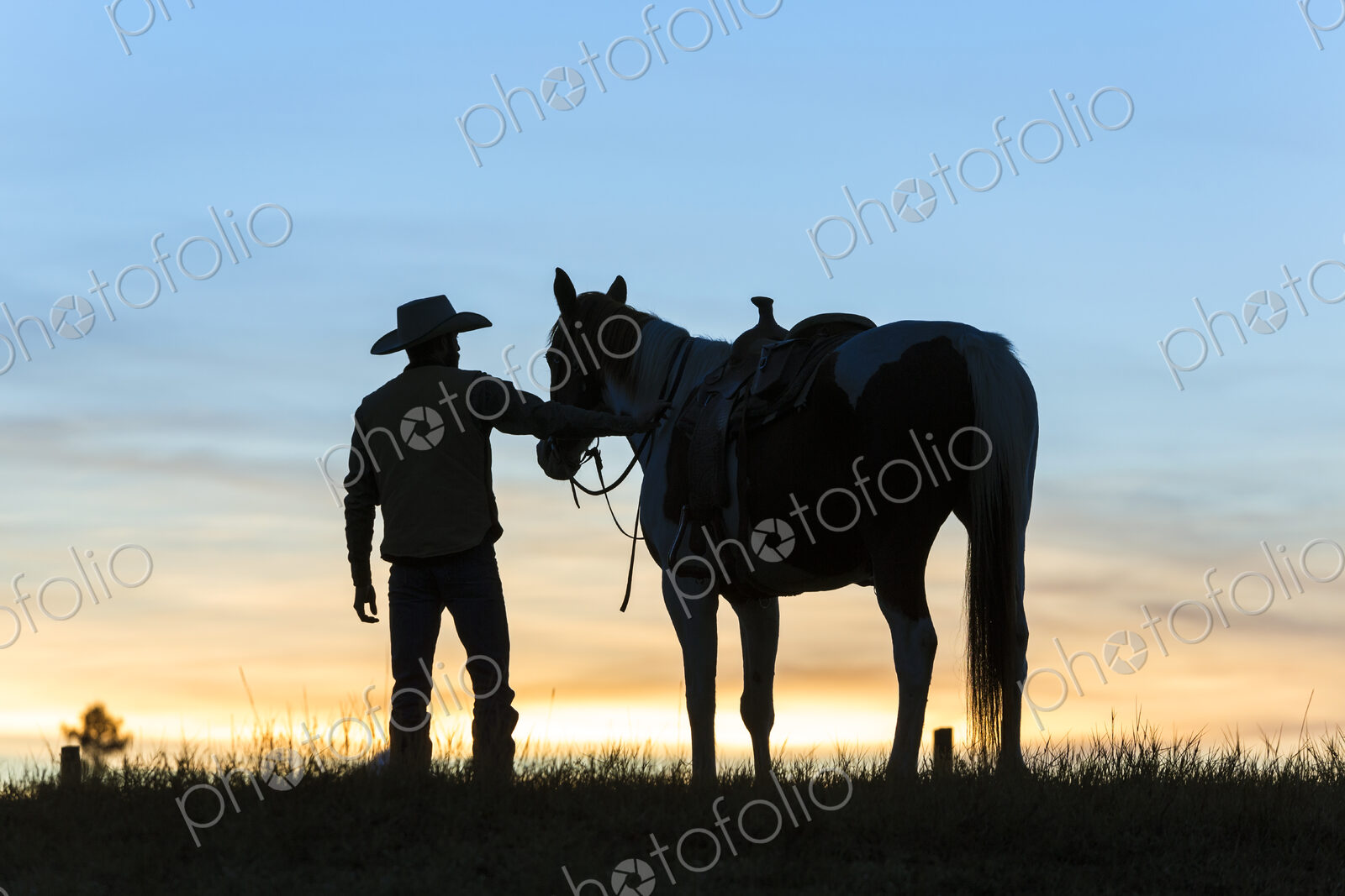 Cowboy standing next to his horse in a Prairie landscape at sunset.
