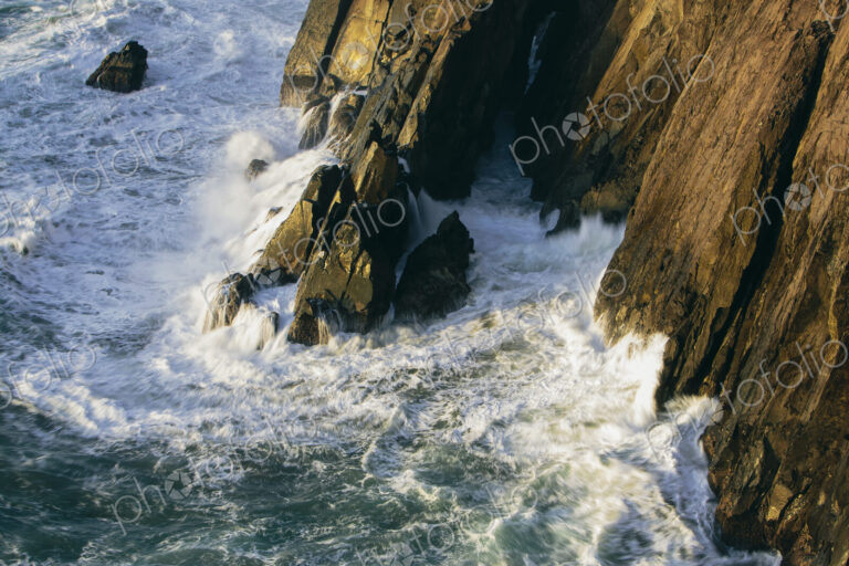 Crashing waves and surf at the base of sheer cliffs on the ocean coastline.