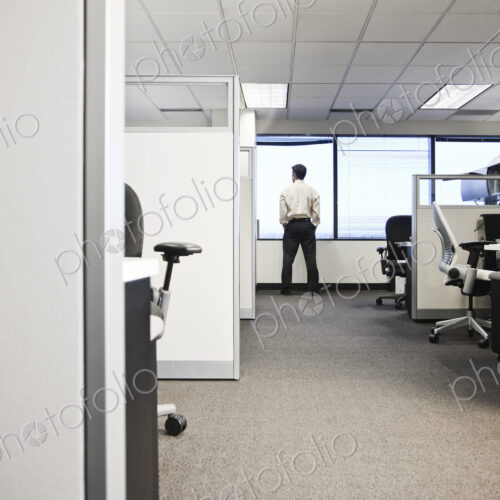 Cubicle office set up with business person at window in background.