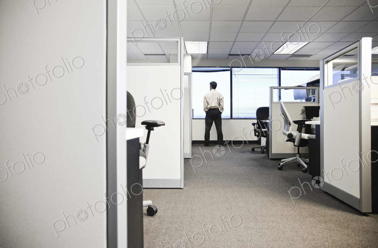 Cubicle office set up with business person at window in background.