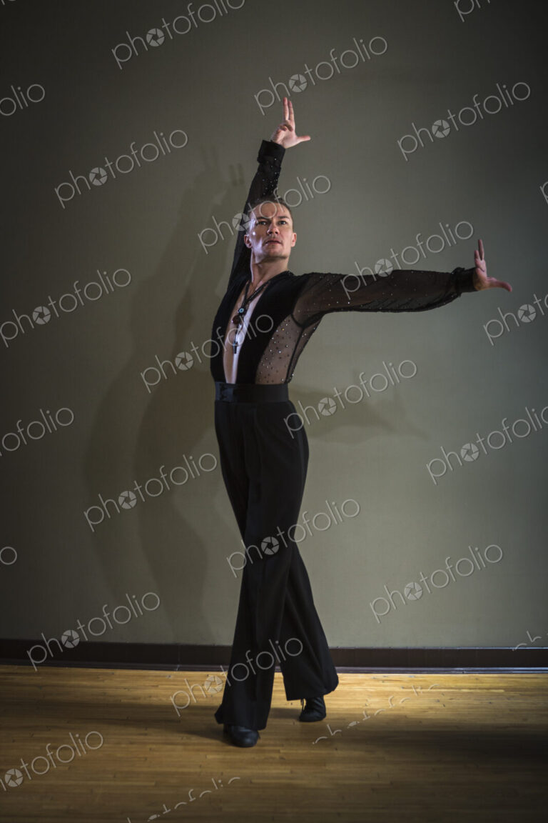 Dancer in dance studio. A man with one arm stretched out and one arm raised.