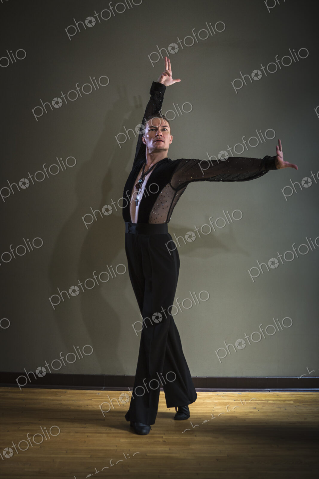 Dancer in dance studio. A man with one arm stretched out and one arm raised.