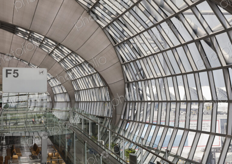 Departure gate at Bangkok Airport, an elevated view of a curved glass terminal wall…