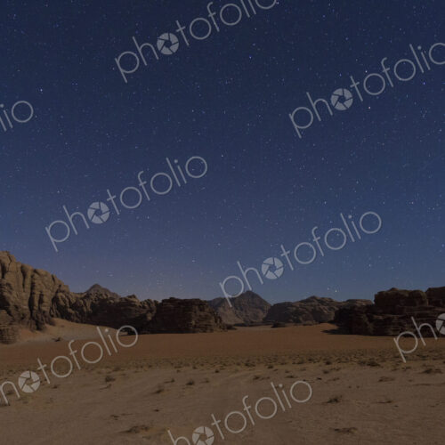 Desert landscape with rocks and mountains under a starry sky in the evening.