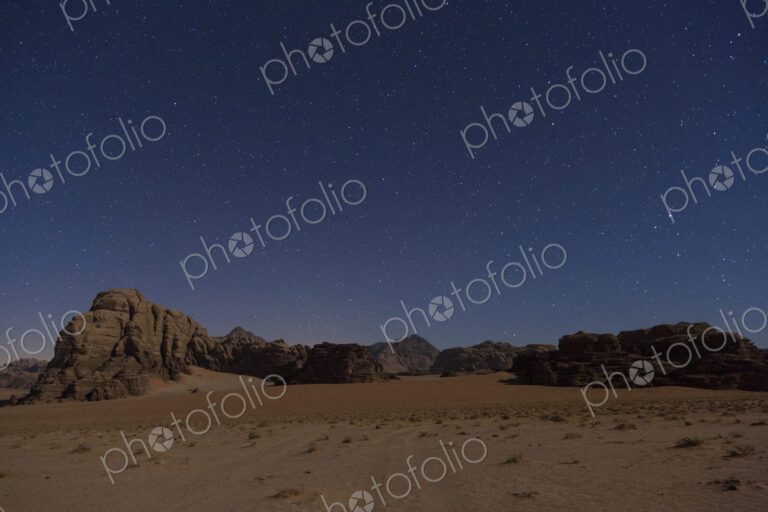 Desert landscape with rocks and mountains under a starry sky in the evening.