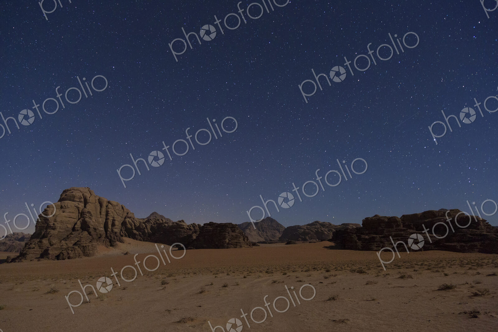 Desert landscape with rocks and mountains under a starry sky in the evening.
