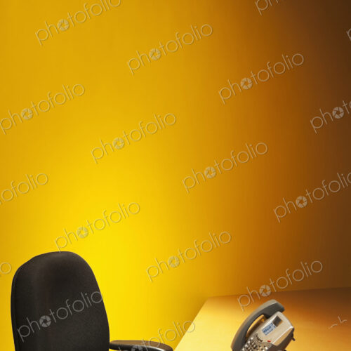 Desk with chair and telephone and yellow wall behind. Desk with chair and telephone and yellow wall behind.