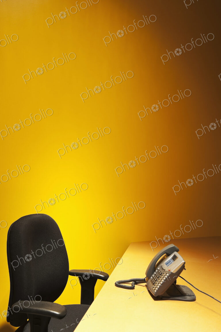 Desk with chair and telephone and yellow wall behind.
