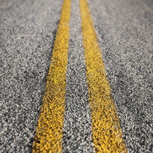 Detailed close-up of yellow double lines painted on an asphalt road, symbolizing… Detailed close-up of yellow double lines painted on an asphalt road, symbolizing…